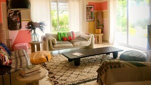 Ein Wohnzimmer mit einer Couch, einem Couchtisch und einem Teppich. Es gibt ein Fenster mit Vorhängen, eine Wandklimaanlage und ein Gemälde.