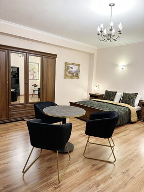 A modern living room with a round table, two black chairs, a sofa, a bed with patterned bedding, a chandelier, and a framed picture on the wall. - Quartier Victoria - Gemütliches Souterrain Apartment Am Goethepark (Weimar)