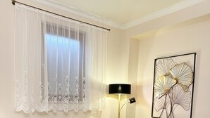 Een woonkamer met een groene bank, een kleine ronde tafel met een vaas rode rozen, een vloerlamp en een abstract kunstwerk aan de muur.