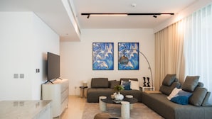 A modern living room with a sectional sofa, a flat-screen TV, a coffee table, and artwork on the wall. - 3BD Haven with Sweeping Water Views (Dubai)