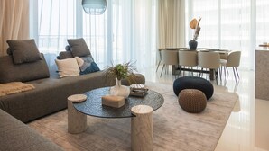 A modern living room with a sofa, round coffee table, and ottoman. There is a dining area with a table and chairs. - 3BD Haven with Sweeping Water Views (Dubai)