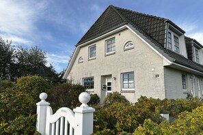 Ein zweigeschossiges Haus mit einer Fassade aus grauem Backstein, einem schwarzen Dach und einem weißen Zaun mit einer kugelförmigen Spitze.