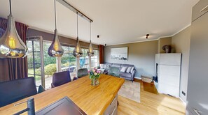 Eine moderne Küche mit einer Holzausziehtheke, hängenden Pendelleuchten und Blick ins Freie durch große Fenster.
