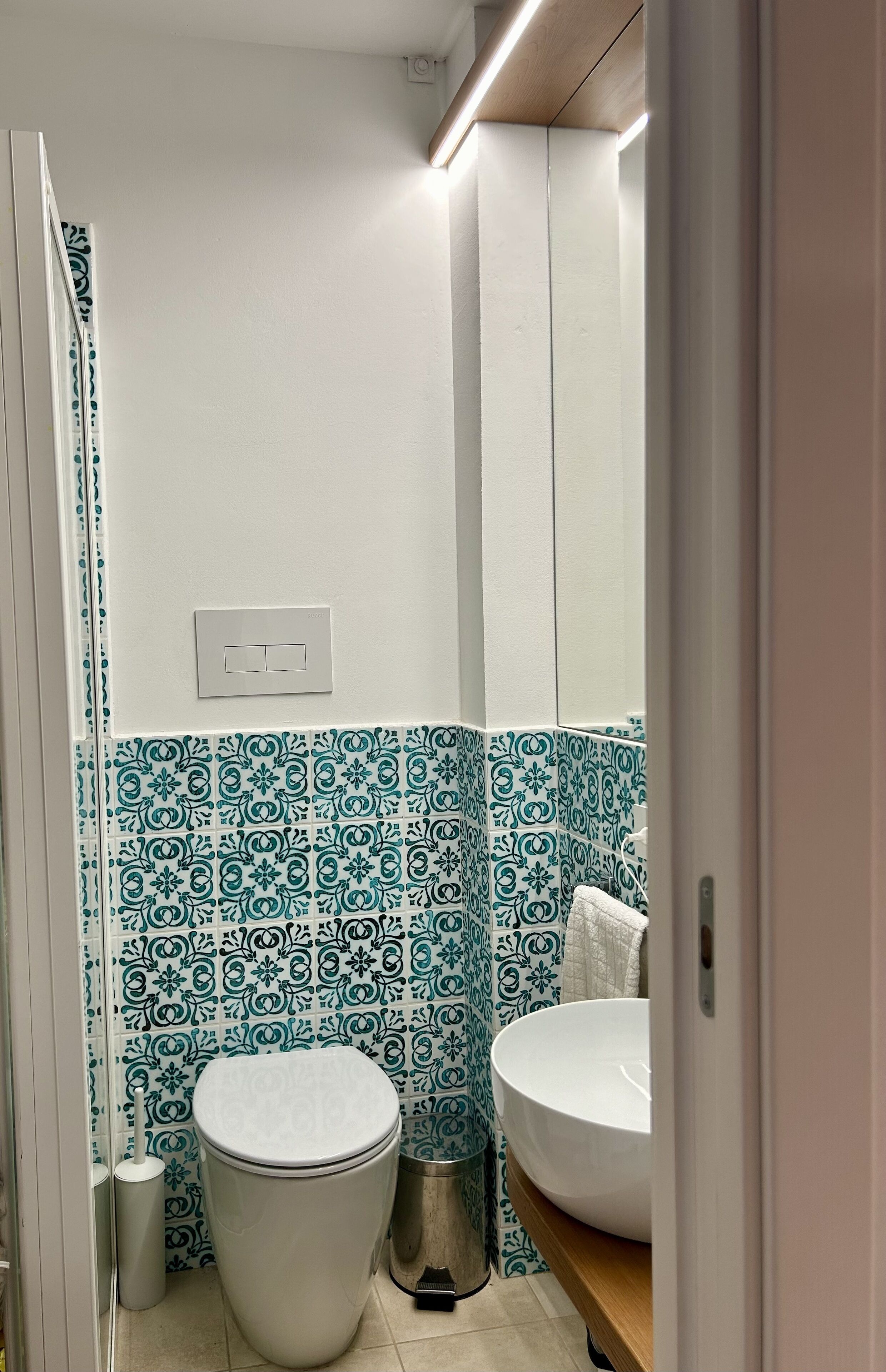 Un baño con inodoro blanco, lavabo con pileta blanca y paredes con baldosas estampadas.