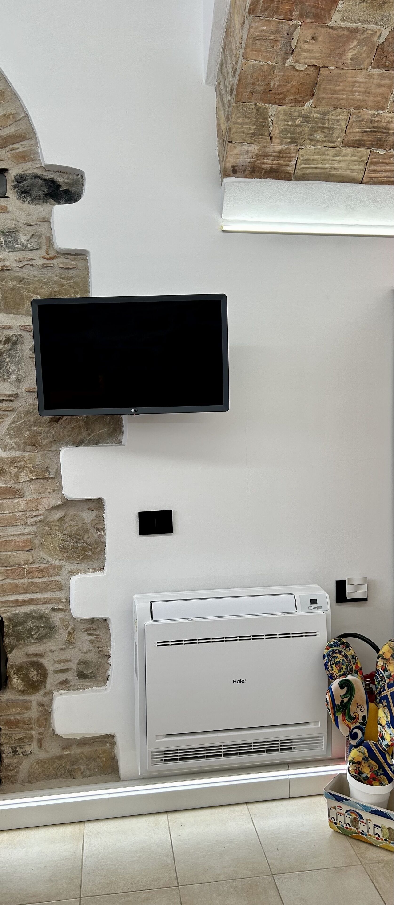 Een kamer met een stenen muur, een wandgemonteerde flatscreen televisie, een witte airconditioning en een kamerbreed tapijt met een patroon op de vloer.