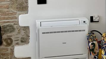 Ein Zimmer mit Steinwand, einem an der Wand befestigten Flachbildfernseher, einer weißen Klimaanlage und einem gemusterten Handtuch auf dem Boden.