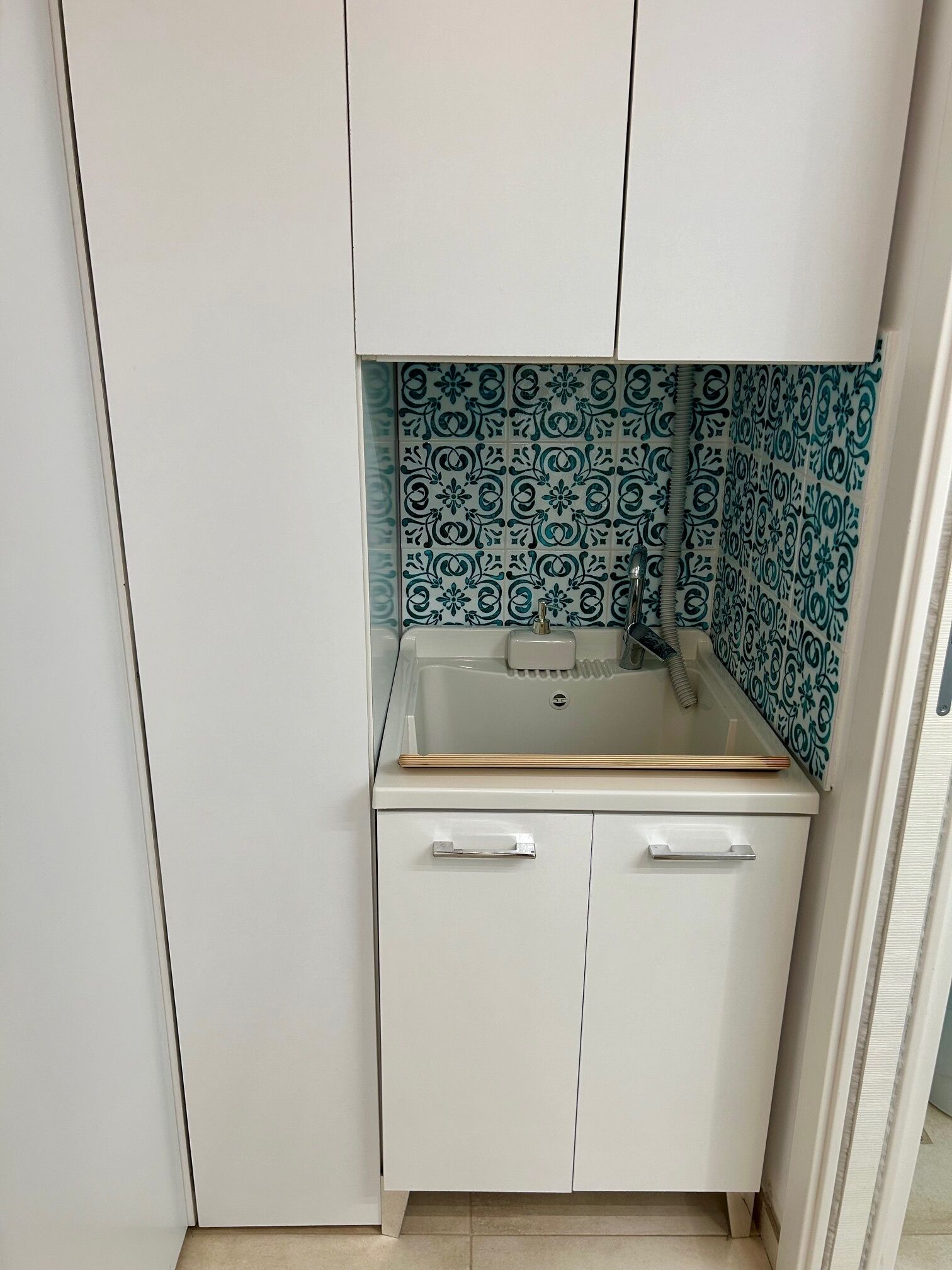 A compact kitchen with a sink, two cabinets, and a patterned backsplash.