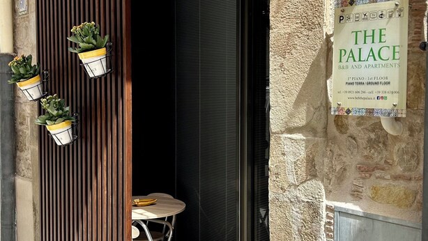 Entrada de un edificio con un cartel que dice 'The Palace B&B and Apartments' y una pequeña mesa con sillas afuera.