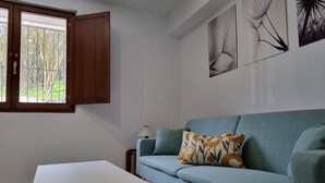 Una sala de estar moderna con un sofá color turquesa, una mesa de centro blanca y una ventana con vistas a árboles.