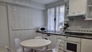 Una cocina moderna con armarios blancos, microondas, lavadora y comedor con mesa redonda y sillas.