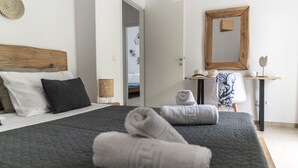 A neatly made bed with a dark quilt, a wooden headboard, and several pillows. There is a small table with a mirror and decorative items. - Bella Casa Pitsidia (Faistos)