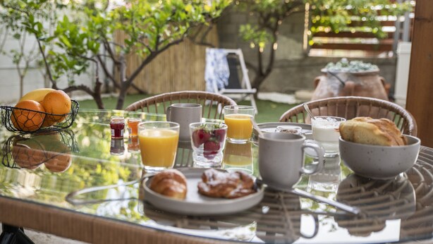 A breakfast table with various food items and drinks, surrounded by wicker chairs and a glass table. - Bella Casa Pitsidia (Faistos)