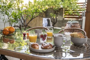 A breakfast table with various food items and drinks, surrounded by wicker chairs and a glass table. - Bella Casa Pitsidia (Faistos)