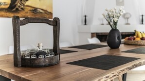 A wooden dining table with a glassware holder, black placemats, and a vase with white flowers. - Bella Casa Pitsidia (Faistos)