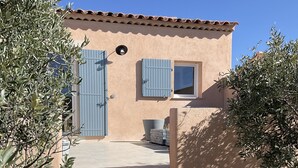 Un edificio con fachada color beige, contraventanas azules y entrada con baldosas.