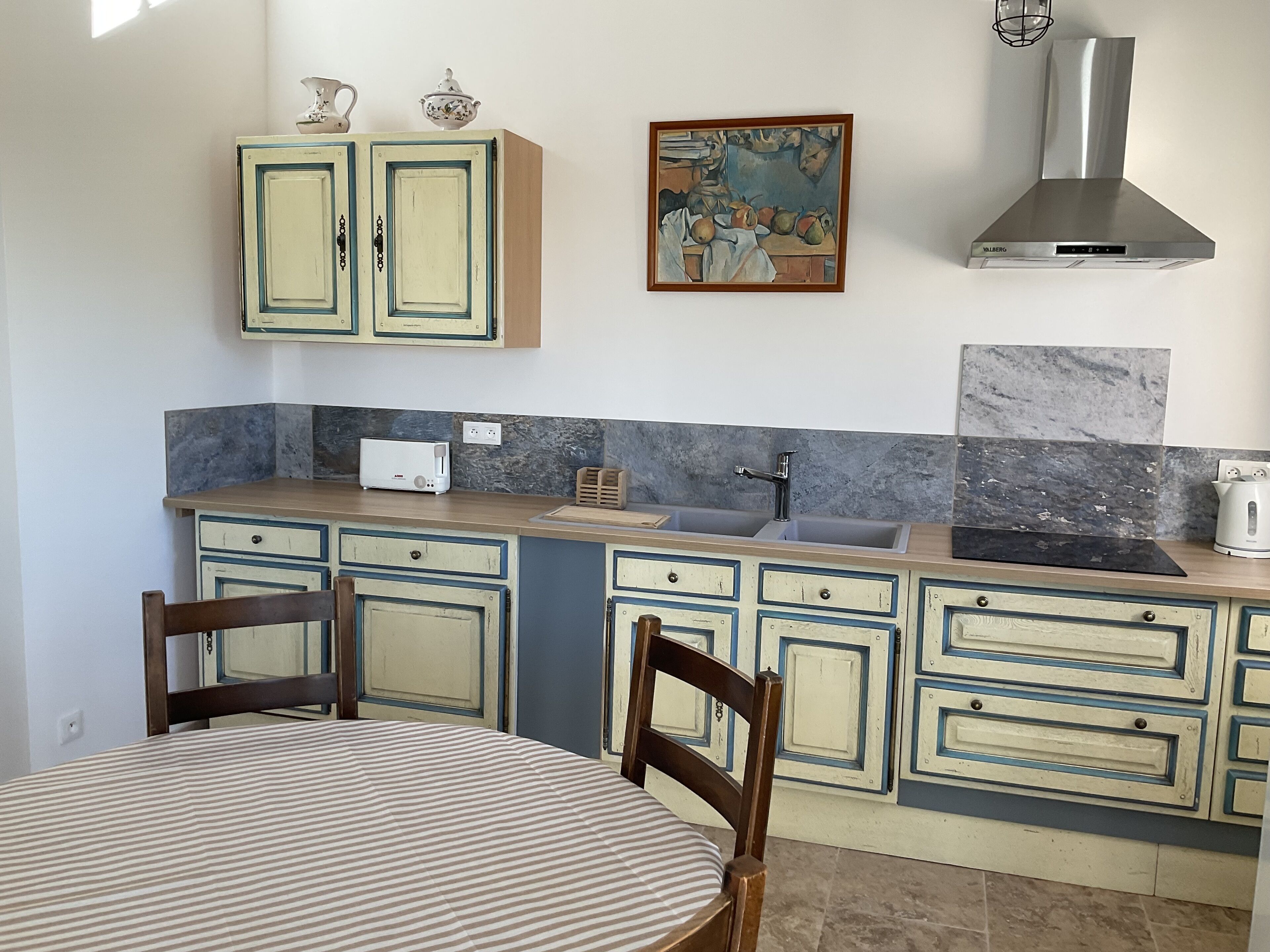 A kitchen with a dining table, chairs, cabinets, a stove, a sink, and a painting on the wall.