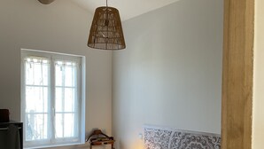 Un dormitorio con una cama, lámpara colgante, ventana y radiador.