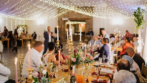 Een balzaal met gedekte tafels voor een formeel evenement, met witte tafelkleden, kaarsen en bloemstukken als decoratie.