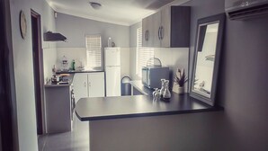 Een compacte keuken met een centraal eiland, een koelkast, een magnetron en een spoelbak. Er staan twee barkrukken bij het eiland.