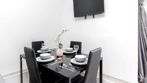 Une salle à manger moderne avec une table noire, des assiettes blanches et des chaises noires. Un téléviseur à écran plat est fixé au mur, au-dessus de la table.