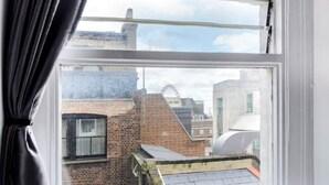 Une vue par une fenêtre, à travers un rideau, donnant sur un bâtiment en briques avec un toit en pente et une structure cylindrique.