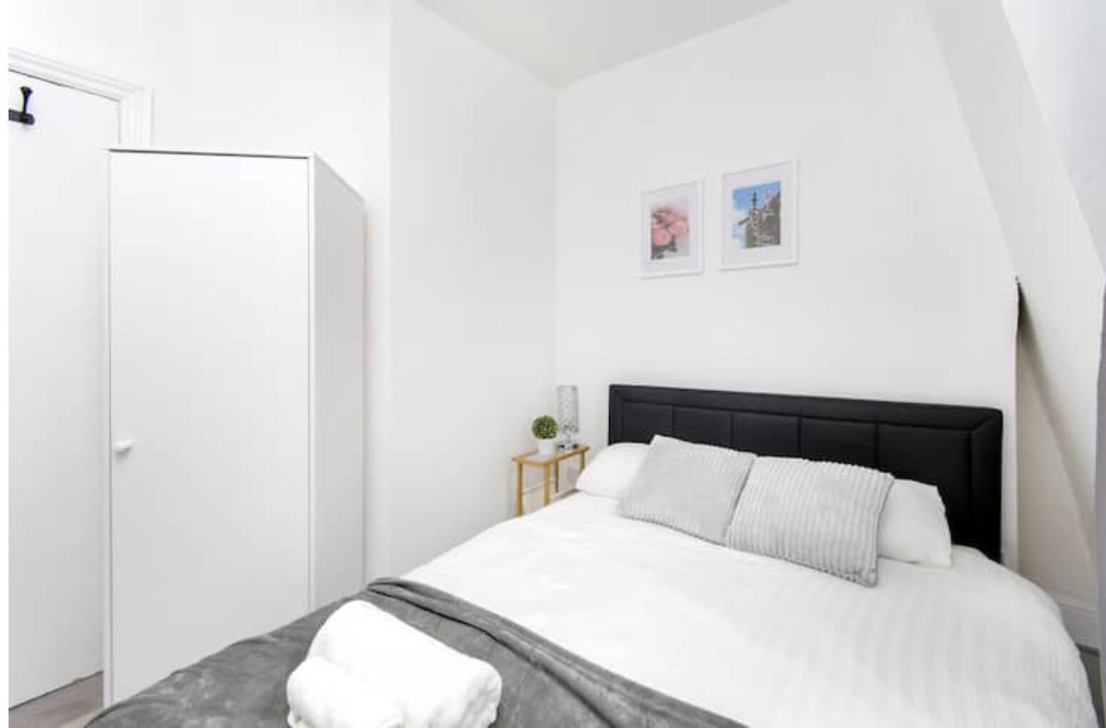 A bedroom with a bed, a wardrobe, and two framed pictures on the wall.