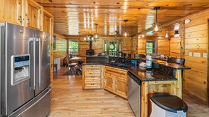 A log cabin-style kitchen with a stainless steel refrigerator, wooden cabinets, a granite countertop, and a central island with a sink. - Tequila Moon: Dive Into Paradise (Sevierville)