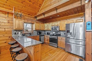 A kitchen with wooden cabinets, granite countertops, stainless steel appliances, and a bar area with stools. - Angel's View: Where the Mountains Look Back (Pigeon Forge)