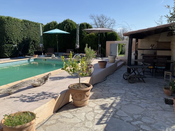 Area piscina con solarium in pietra, piante in vaso, mobili da esterno e ombrelloni.