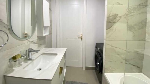 Uma casa de banho moderna com um espelho grande, duas lavatórios, uma sanita e uma máquina de lavar roupa.