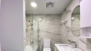 Ein modernes Badezimmer mit einer gläsernen Duschkabine, einer weißen Toilette und einer Wand mit Marmorfliesen.