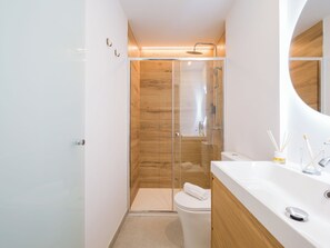A modern bathroom with a glass-enclosed shower, a white toilet, and a wooden vanity with a mirror. - Shabolo Apartments las Palmas (Las Palmas de Gran Canaria)