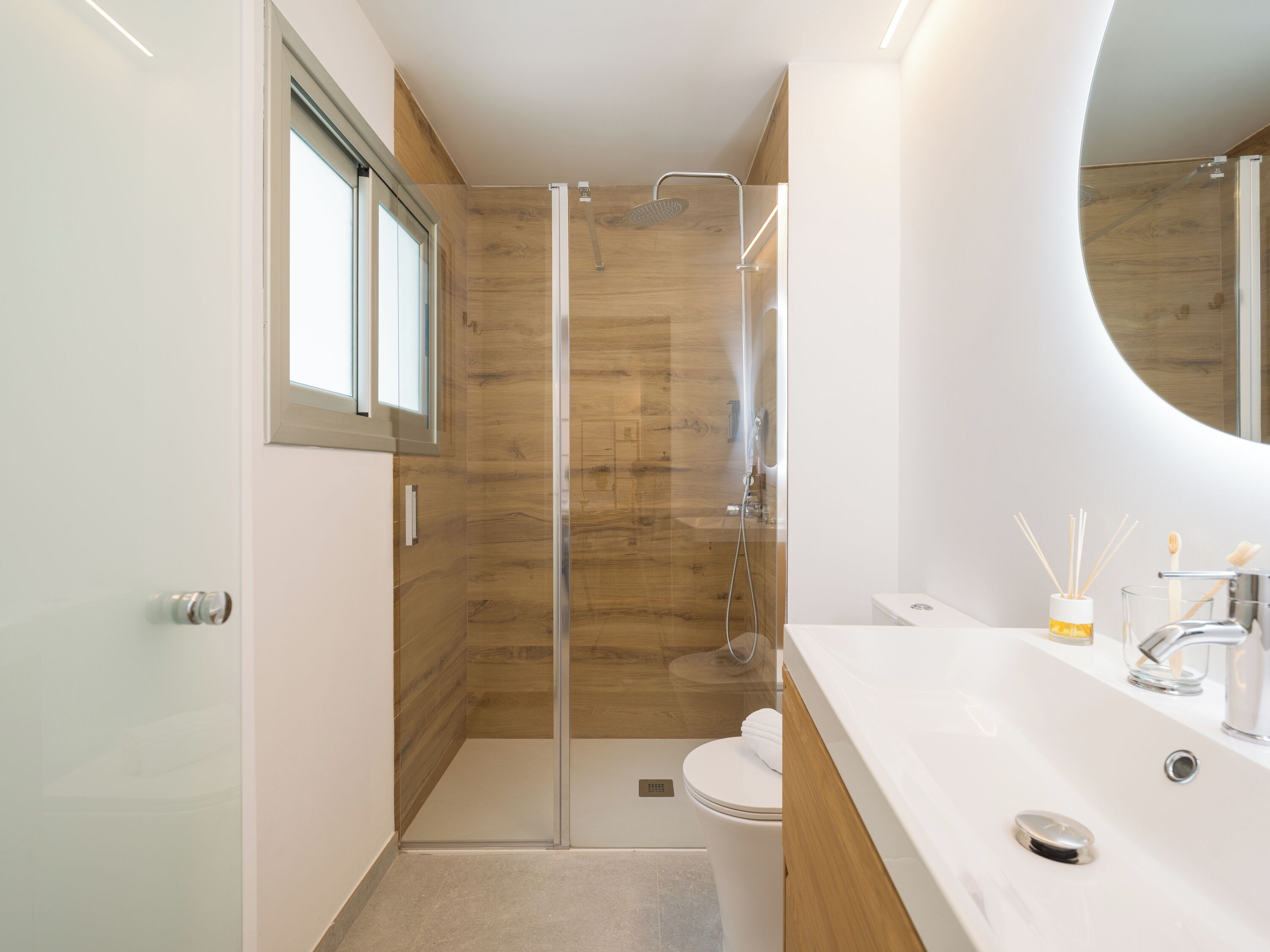 A modern bathroom with a glass-enclosed shower, a white sink with a mirror, and a toilet.