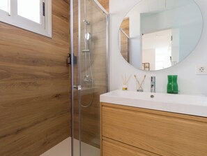 A modern bathroom with a glass-enclosed shower, wooden panel walls, a white vanity with a mirror, and a green vase on the counter.