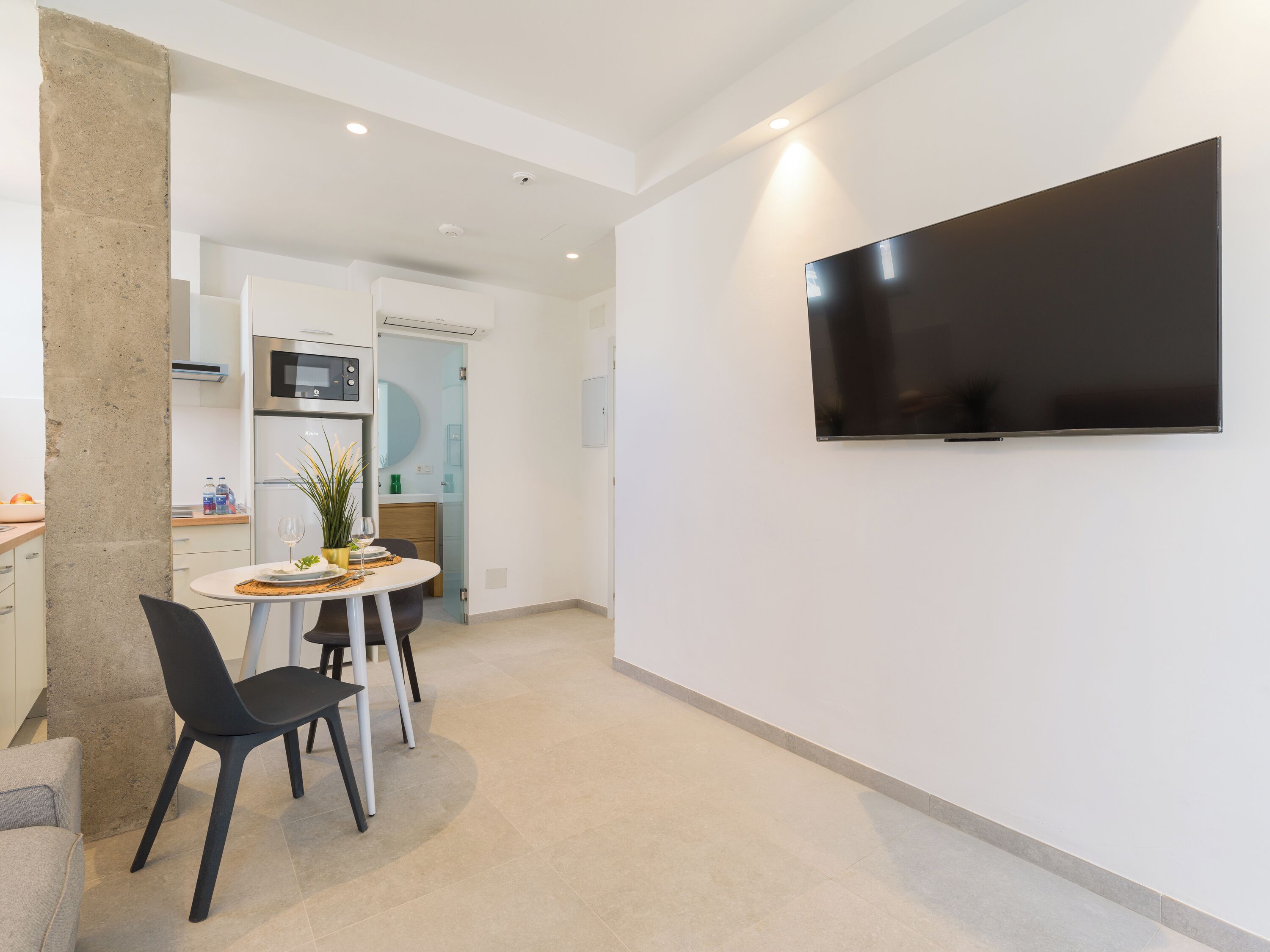 Eine moderne Küche mit integriertem Mikrowellenofen, einem Essbereich mit rundem Tisch und Stühlen sowie einem an der Wand montierten Flachbildfernseher.