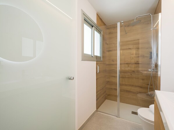 A modern bathroom with a glass shower enclosure, a toilet, and a sink.