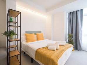 A neatly arranged hotel room with a bed, a shelf with plants, and a window with curtains. - Shabolo Apartments las Palmas (Las Palmas de Gran Canaria)