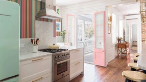 A kitchen with a stove, oven, and a striped backsplash. There is a door leading to a balcony with a railing. - Casa Zoë | Royal Cottage I – Designer Escape (Charleston)