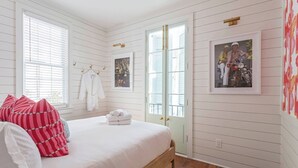 A bedroom with a bed, white walls, a door, and a framed picture on the wall. - Casa Zoë | Royal Cottage I – Designer Escape (Charleston)