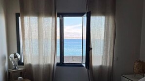 Un dormitorio con cama, una mesita de noche con lámpara y vista al mar a través de un ventanal grande.