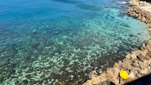 Vista costera con agua azul cristalina, costa rocosa y un pueblo distante.
