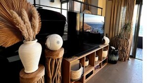 Una sala de estar moderna con un televisor de pantalla plana grande, muebles de madera y vista al mar a través de amplios ventanales.