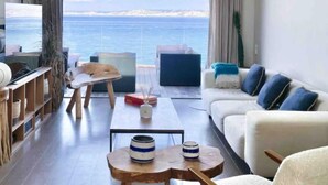 Una sala de estar moderna con vista al mar, que incluye un sofá, una mesa de centro y mesas auxiliares de madera.