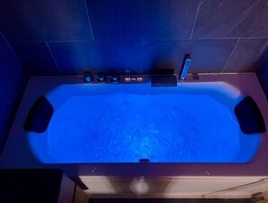 Et moderne badekar med et digitalt kontrolpanel foran mørke fliser.