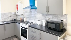 Una cocina compacta equipada con estufa a gas, horno, microondas y una campana extractora azul.