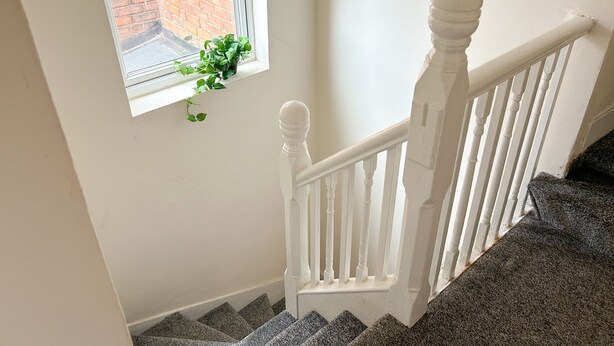 Una escalera con balaustres blancos y un ventanal con una planta en maceta.