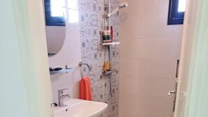A small bathroom with a white sink, a shower, and a patterned wall.