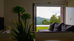 Ein Zimmer mit einer Couch, die einem großen Fenster zugewandt ist, einer Zimmerpflanze und einem Fernseher auf einem Schrank.