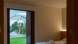 Ein modernes Schlafzimmer mit Bett, einer Schiebetür zu einem Außenbereich und einer kleinen Sitzecke mit Stühlen und Tisch.