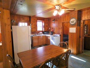 A wooden cabin-style kitchen with a refrigerator, stove, microwave, and sink.
